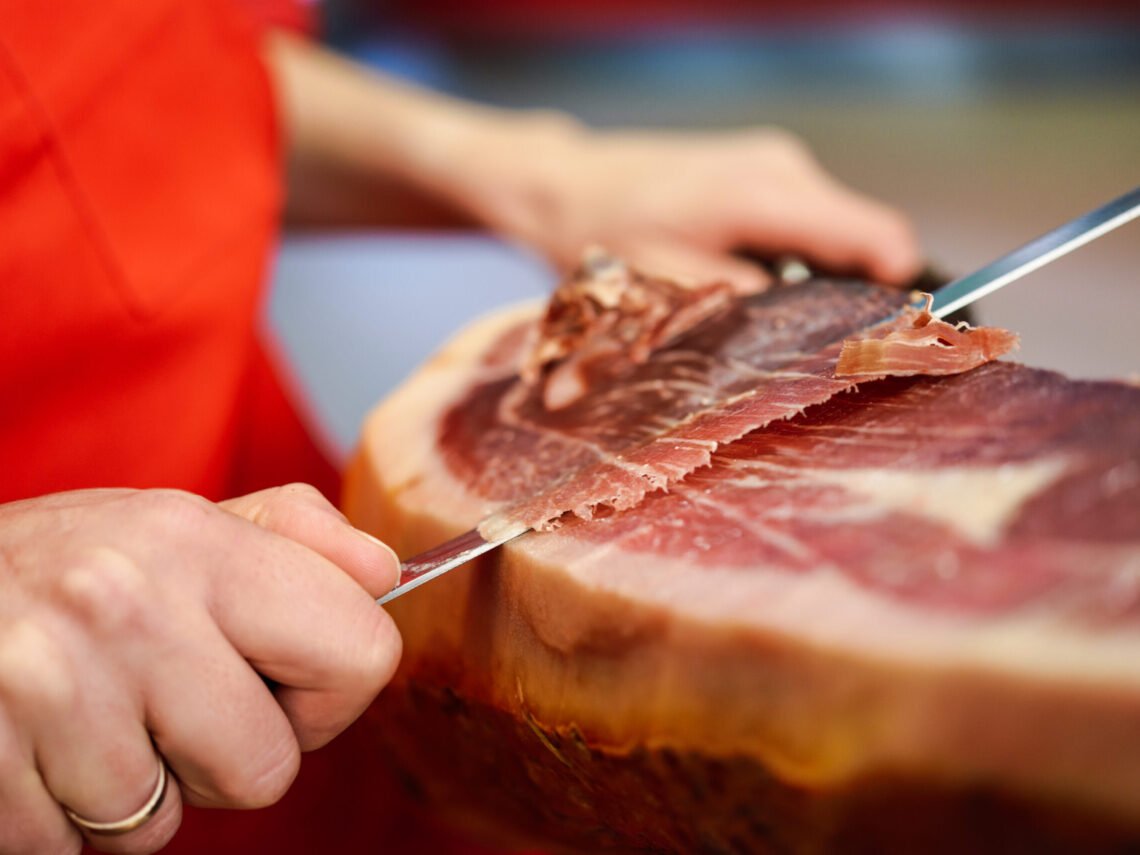 Professional cutter carving slices from a whole bone-in serrano